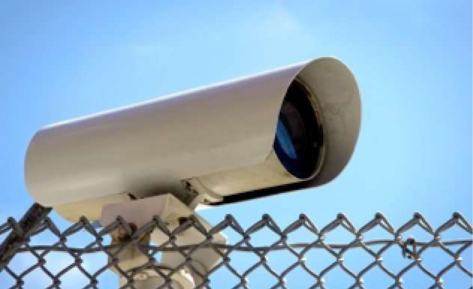 A cctv camera on a pole above a chain link fence